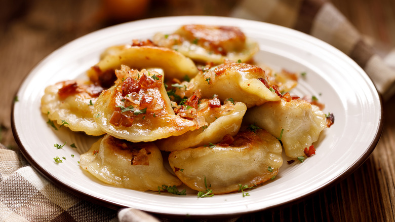 A white ceramic plate of fried pierogis, Polish dumplings, sprinkled in chives