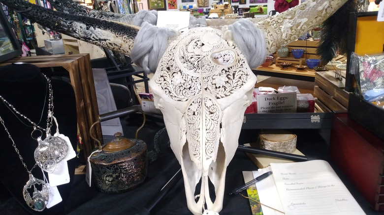 A table with a carved skull, jewelry, and art on the walls of the Milton's Artist Guild interior