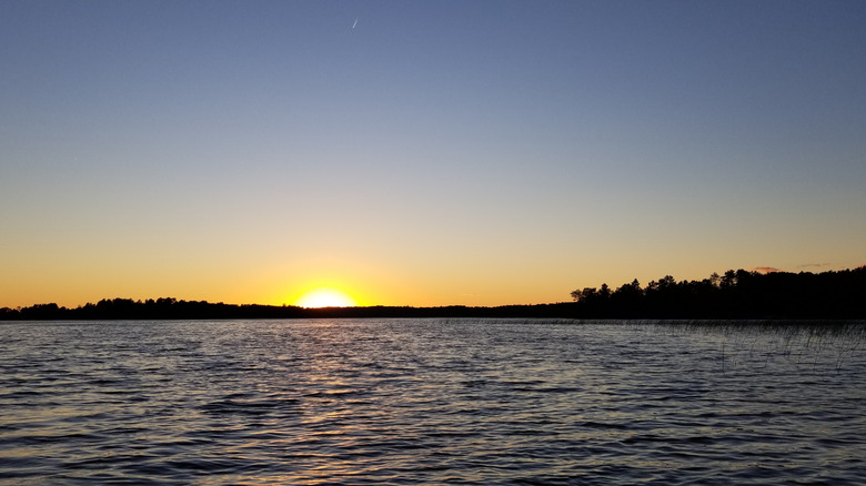 A sunset over a lake near Cohasset with the light reflecting on the water and a silhouette of the trees in the distance