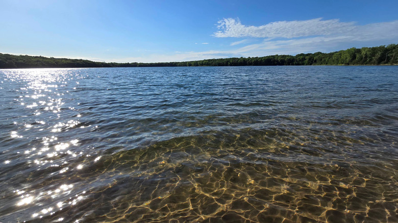 Clear water with sunlight on it with trees in the distance and a blue sky at Little Carnelian Lake, Minnesota