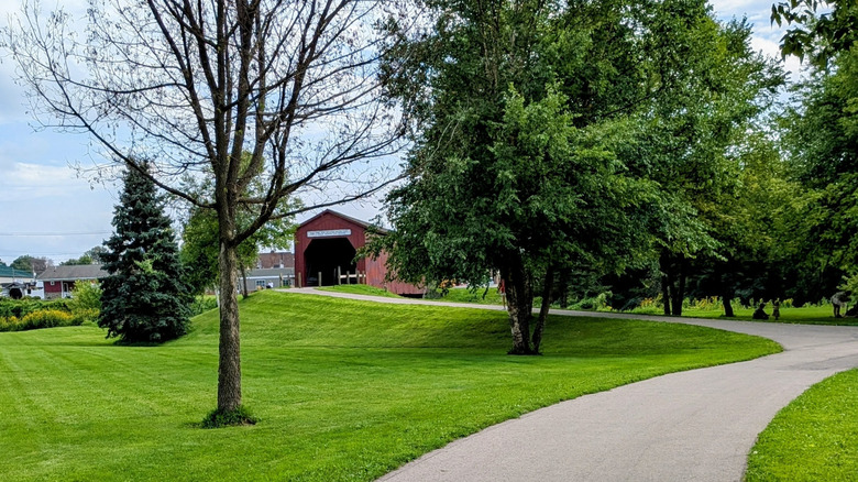 Paved trail leading through trees to covered bridge in a park in Zumbrota