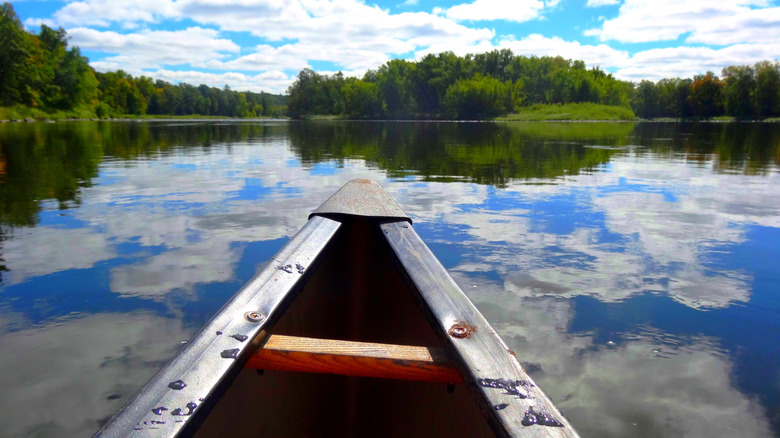 Bow of canoe on water with sky reflected in lake