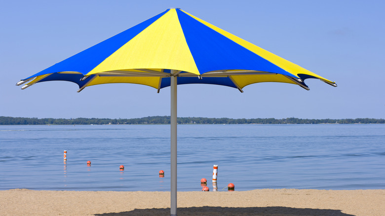 a blue and white striped beach umbrella on a sandy beach by a lake