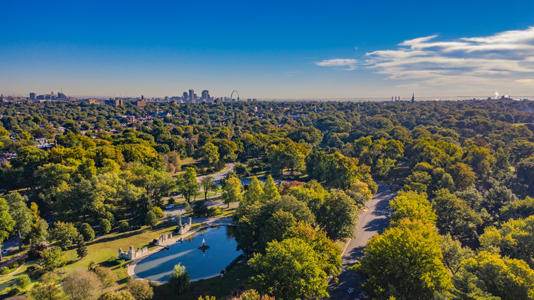 Lush trees, water features, and a paved trail at Tower Grove park, with the St. Louis skyline in the background