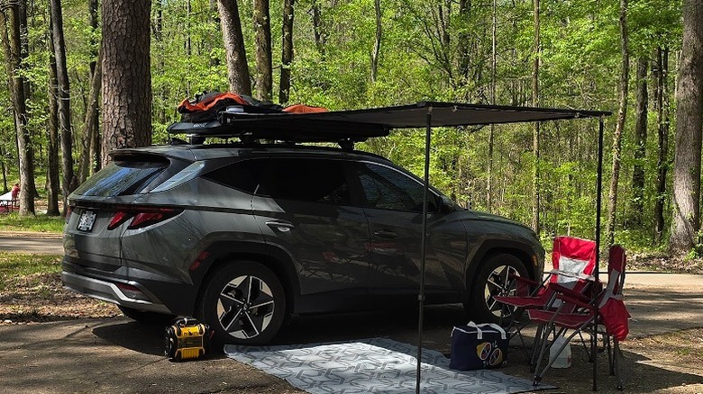 The beginnings of a campsite at the Rocky Springs Campground with a car, awning and chairs in amongst the trees.