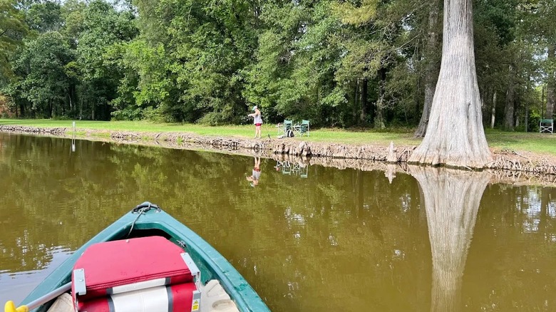 Views of the front of a kayak drifting along a creek with a person fishing from the shoreline at Leroy Percy State Park in Mississippi.