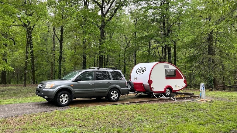 A red and white teardrop camper hitched to a gray SUV, at the wooded campsite at Leroy Percy State Park in Mississippi.