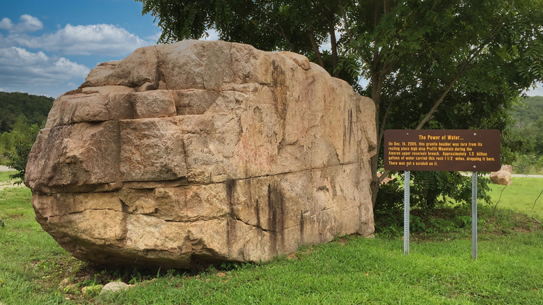 huge beige boulder in field next to sign