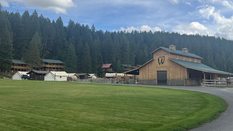 A field of grass in front of Bar W Guest Ranch barn and lodgings, with a forest in the background