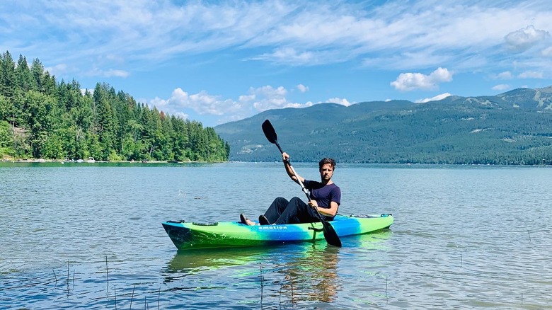 man in kayak on lake with green mountains in the background