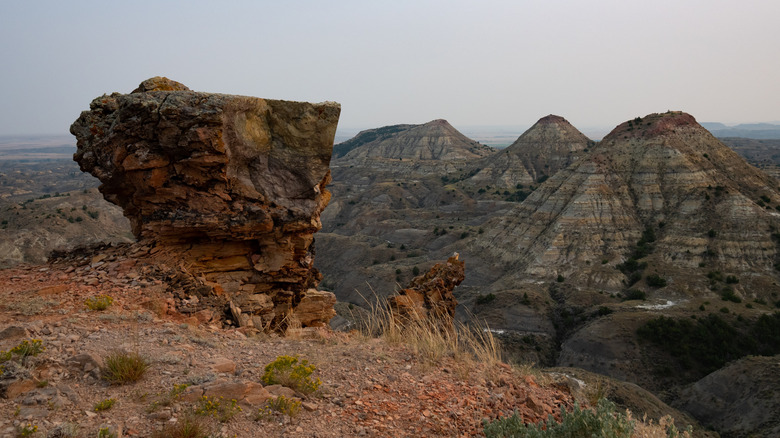 Orange rock formation and orange shale in foreground with striped gray mountains in background and overcast sky above