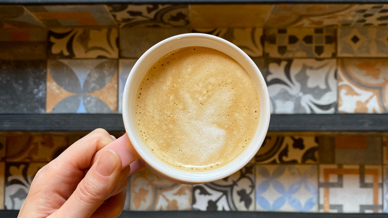 A woman's hand holding a cappuccino over colorful Moroccan tiles