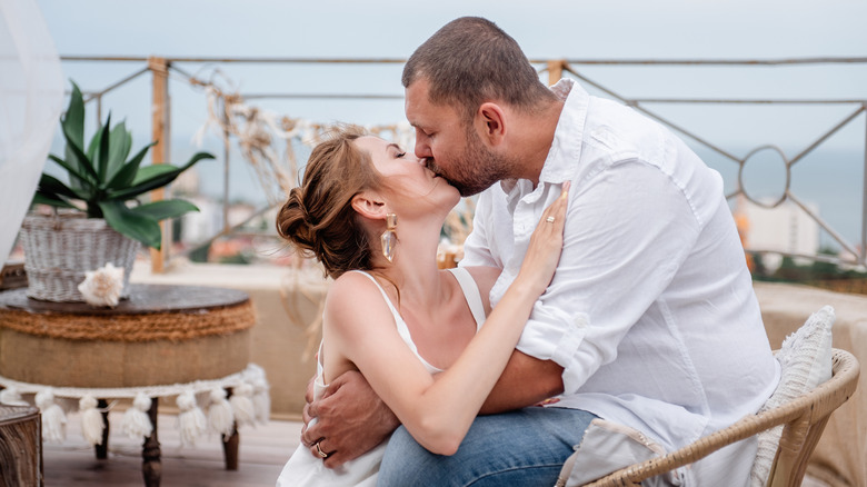 A young attractive couple dressed in white kissing on the lips on an open terrace of a restaurant