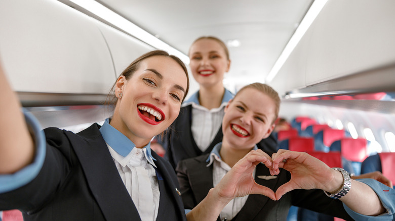 Three female flight attendants posing for a selfie on an empty plane.