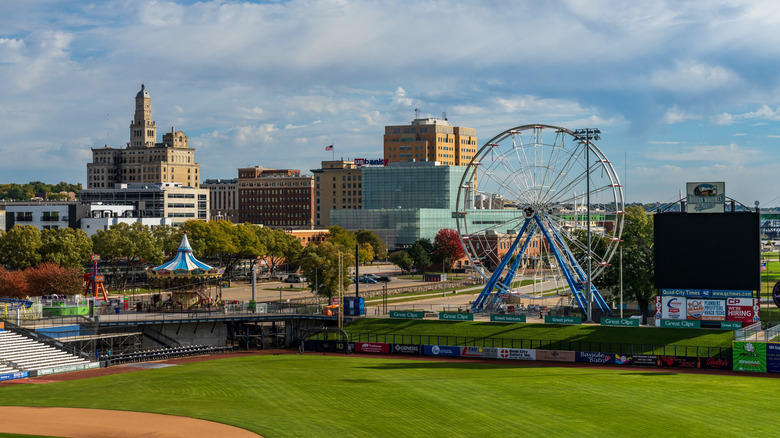 View of Modern Woodmen Park in Davenport, IA with Ferris Wheel and other amusement park rides visible, with downtown skyline the background