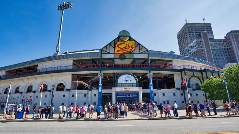 People gather outside to attend baseball game at Sahlen Field with downtown Buffalo, New York in the background