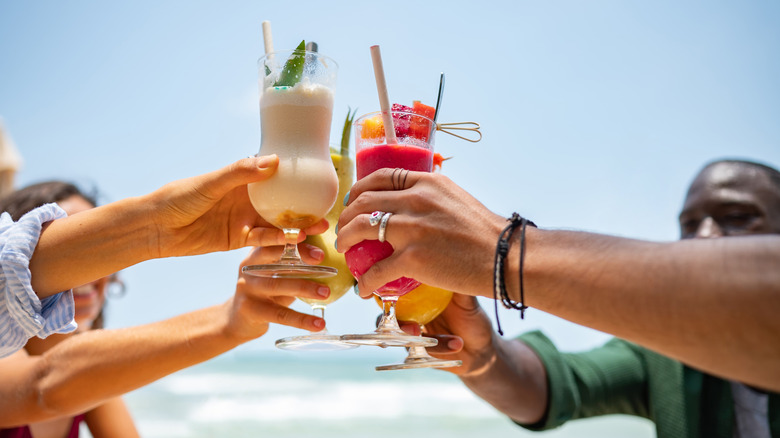 A group of people toasting with cocktails on the beach.