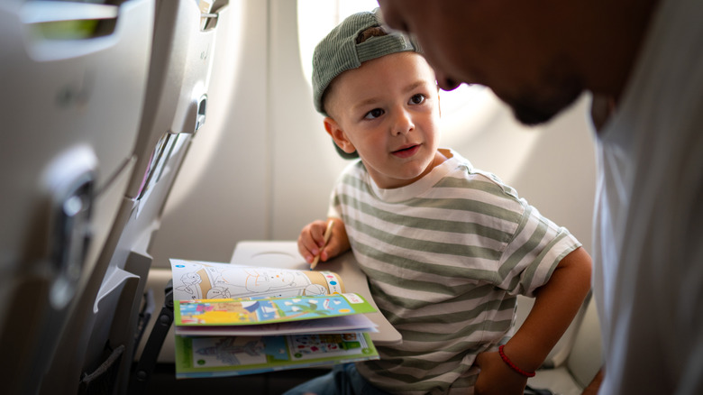 Little boy looking at his parent as he colors in a coloring book on a tray table on a plane