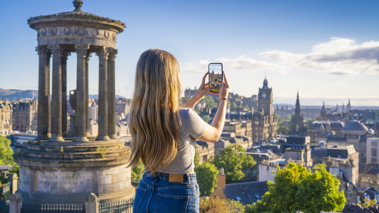 A woman taking photos of Edinburgh from the top of Carlton Hill