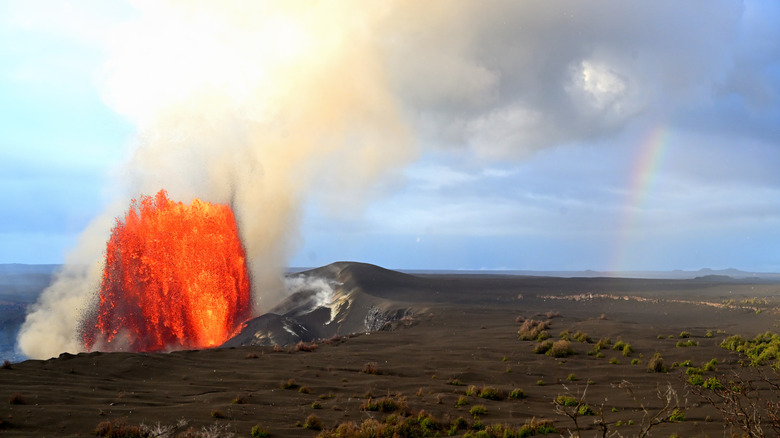 Molten red lava erupting from black lava fields with a rainbow to the right