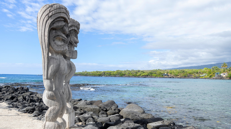 Carved wooden tiki statues at Puʻuhonua o Hōnaunau National Historical Park overlooking the bay