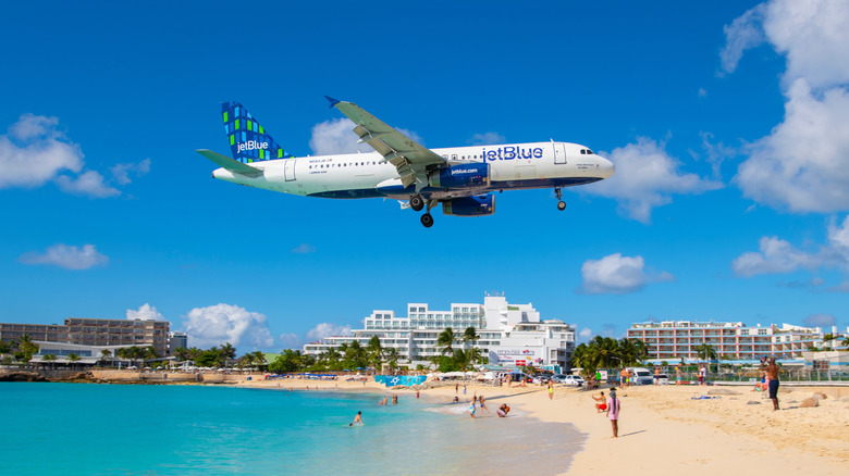 A JetBlue airplane flying low over Maho Beach's blue waters and white sand