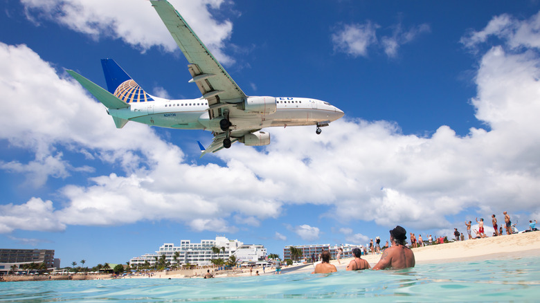 A United plane lands near Sint Maarten's Maho Beach as swimmers float in the blue water