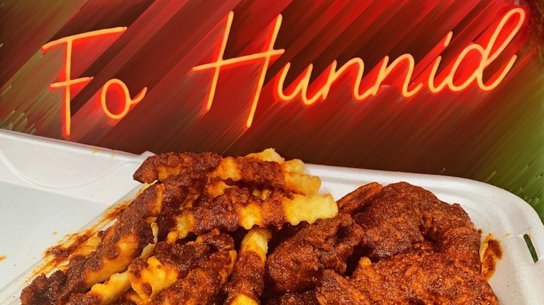 Neon sign reading "Fo Hunnid" behind a container of Nashville hot chicken and fries