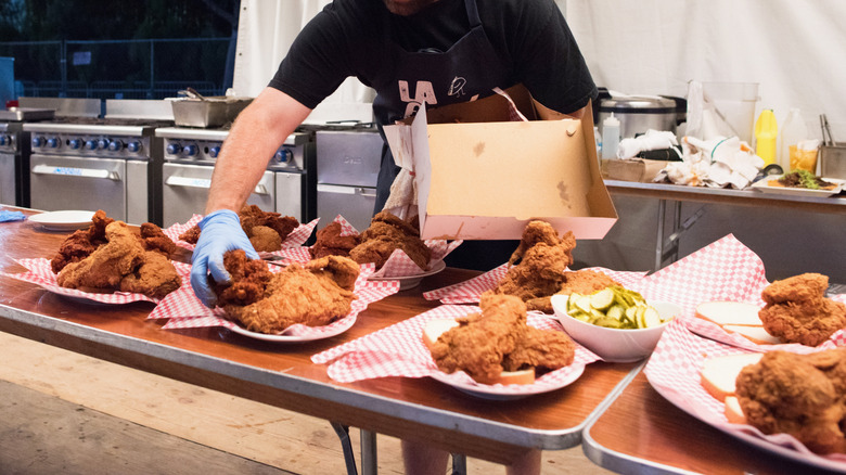 A cook plating hot chicken on tables in kitchen
