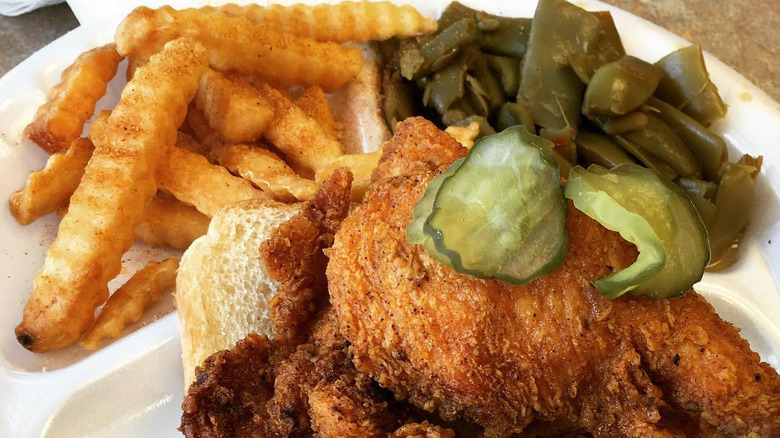 A plate of Nashville hot chicken with pickles, fries, and green beans