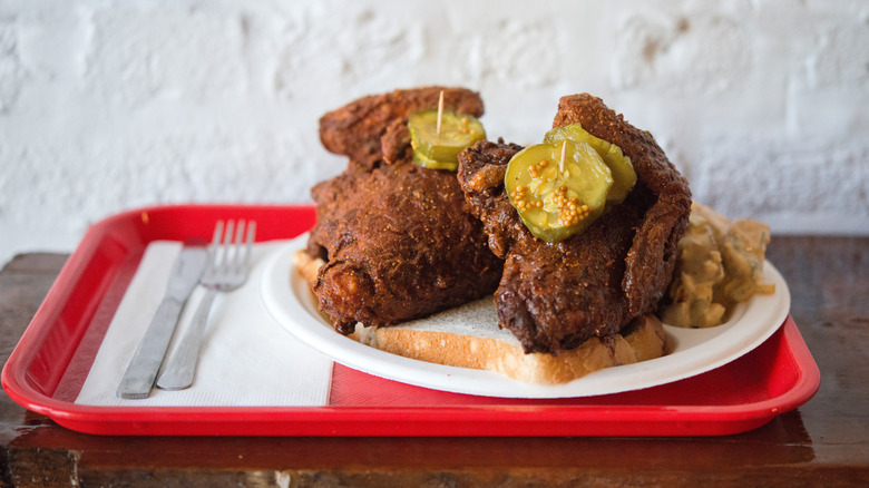 hot chicken pieces with pickles on a red tray