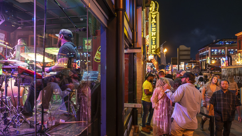 A musician plays inside a venue in Nashville while music lovers gather outside to get in