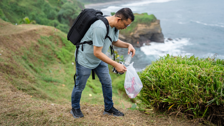Mature male walking through a beach pause to pick up litter