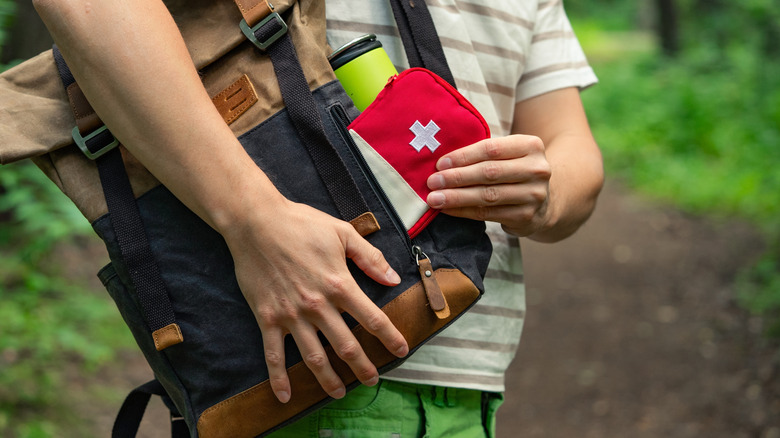 Close-up of a person taking a first aid kit out of a backpack while on a forest trail