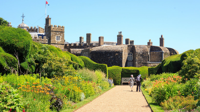 Two people strolling up a path flanked by flowerbeds in the grounds of Walmer Castle in Walmer, Kent