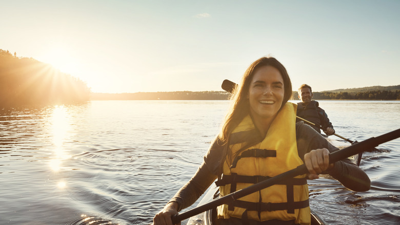 A smiling woman wearing a life jacket paddles on a river.