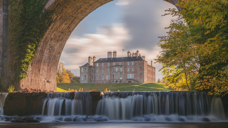 Dalkeith Palace seen through an archway with a waterfall and trees in the foregournd