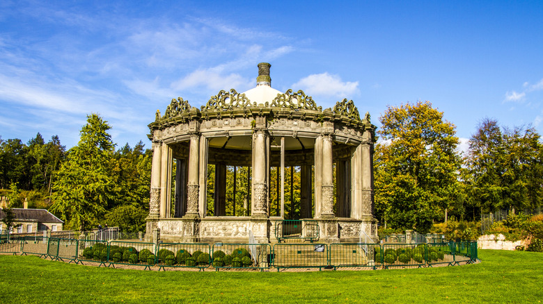 Historic circular conservatory with stone columns against blue sky surrounded by trees Dalkeith Country Park