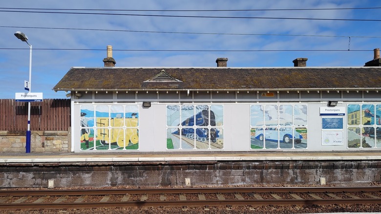 Prestonpans train station with mural of trains against blue sky with clouds.