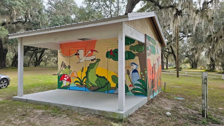 A small building covered with a mural of colorful wetland animals is surrounded by moss-draped trees at Little Orange Creek Preserve in Florida.