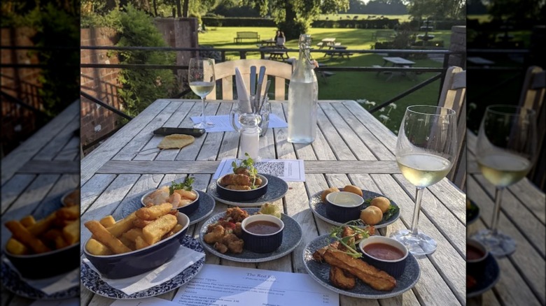 Wooden table with two wine glasses and various appetizers overlooking a green lawn