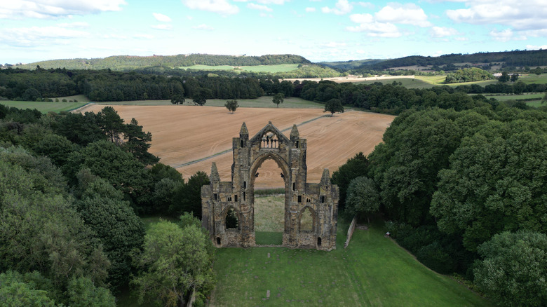 The ruins of Gisborough Priory surrounded by trees with a wheat field behind them in Guisborough, England