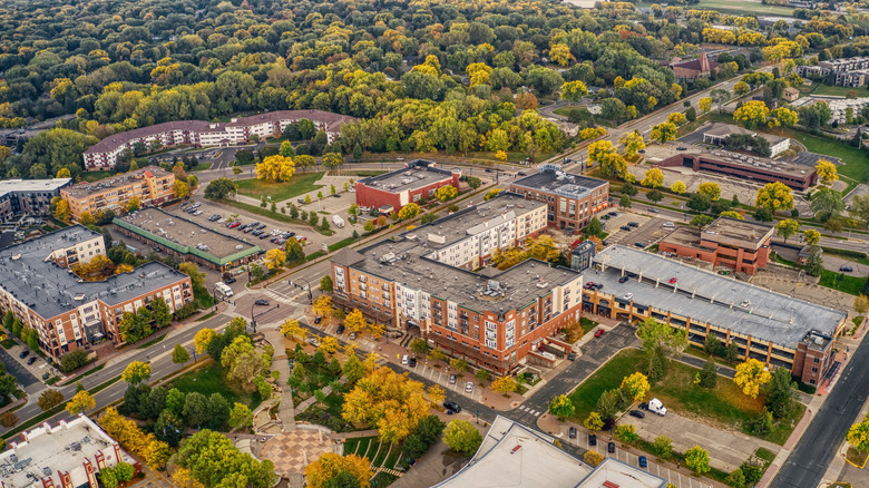 An aerial photo above a few blocks in Burnsville with old brick buildings, streets lined with trees, and forest in the distance