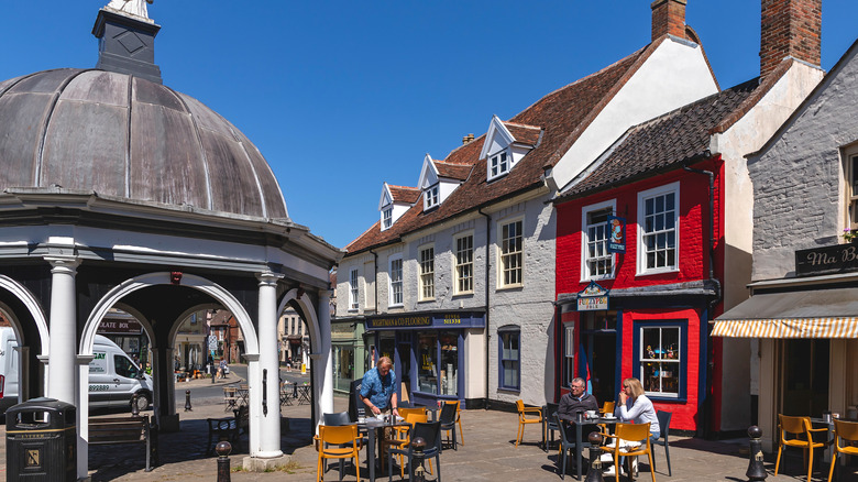 People sitting at tables in the sunshine outside restaurants beside the Butter Cross in Bungay, England