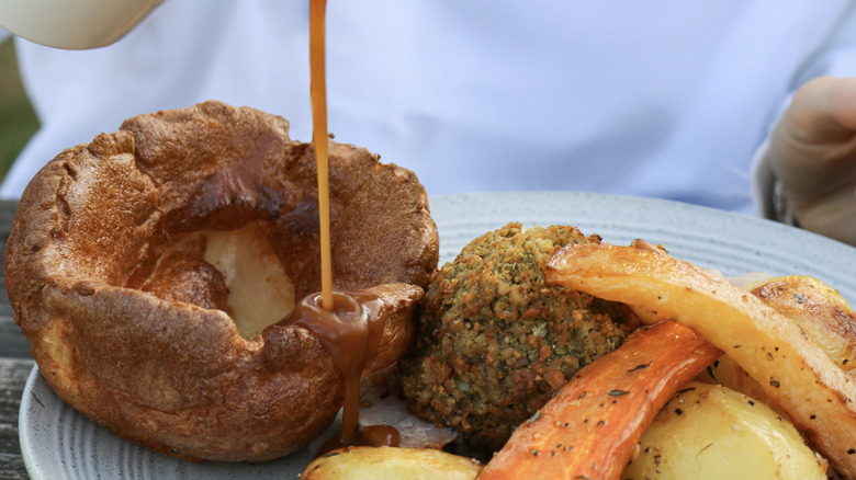 Yorkshire pudding, roasted potatoes, carrots, and stuffing, with gravy being poured over the plate.