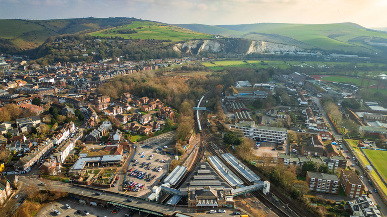 Aerial shot of Lewes' town sprawl including houses, railway lines, parking lots, medieval streets and surrounding green hillsides and forests