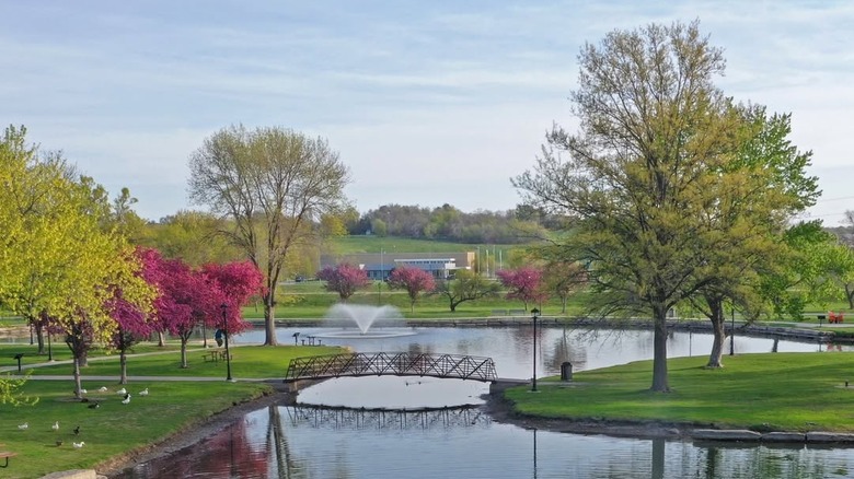 Halleck Park in Papillion, Nebraska, with a bridge over a lake surrounded by trees and a fountain in the background
