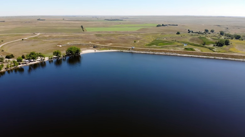 Lake with beach and trees on shoreline, with fields behind, at Box Butte Reservoir