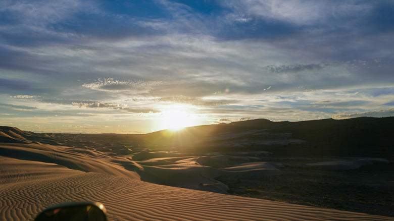 Sand dunes extend into the horizon as the sun sets