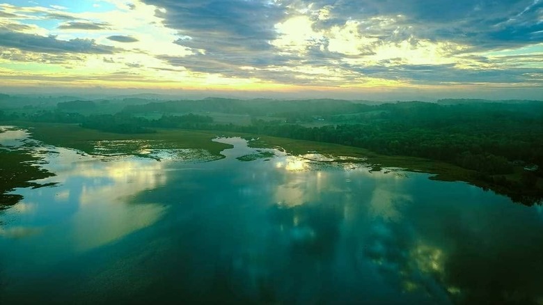 Aerial shot of Knox Lake, with clear water surrounded by trees, hills, and greenery under a cloudy sky